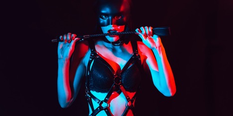 Masked Mistress is biting on a leather crop